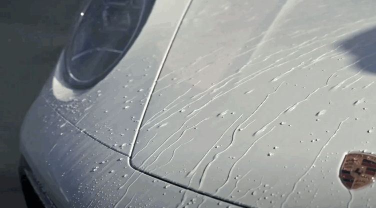 Close-up of water droplets beading and running off the hood of a white Porsche, demonstrating the hydrophobic effect of paint protection film.