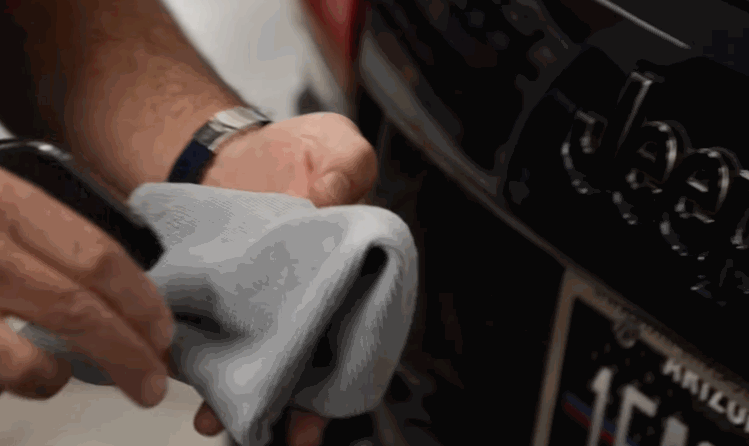 Ceramic coating application: A person in a workshop cleans the rear emblem of a black Jeep with a microfiber cloth and a spray bottle, preparing the surface for ceramic coating.