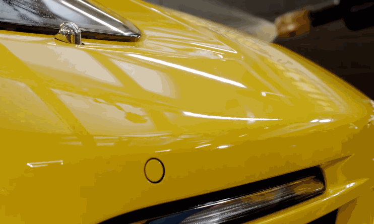 Ceramic coating buffing: A person in black gloves polishes the hood of a yellow sports car with a dual-action polisher and a white foam pad, applying a liquid ceramic coating for long-lasting protection.