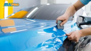 A technician smoothing out vinyl wrap on a blue car, carefully applying the material for a smooth and even finish.