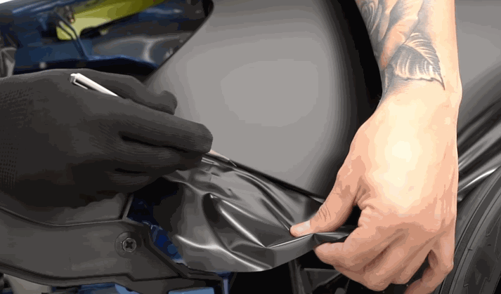 A close-up of a person cutting black vinyl wrap during the application process on a vehicle panel.