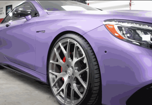 A purple car being wrapped with vinyl, showing the large sheet of material being applied to the vehicle's body.