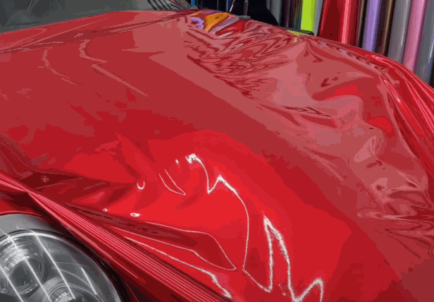 A red car hood covered with vinyl wrap, showing the smooth and shiny surface after the material has been applied.