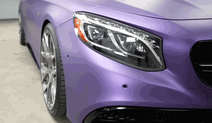 Close-up of a person using a precision knife to trim purple vinyl wrap along the edge of a car panel during a vehicle wrap installation.