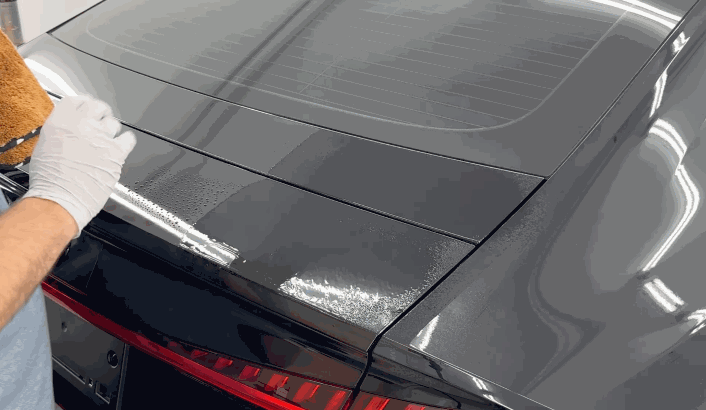 Technician wiping down a glossy black trunk with a microfiber towel during ceramic coating removal.