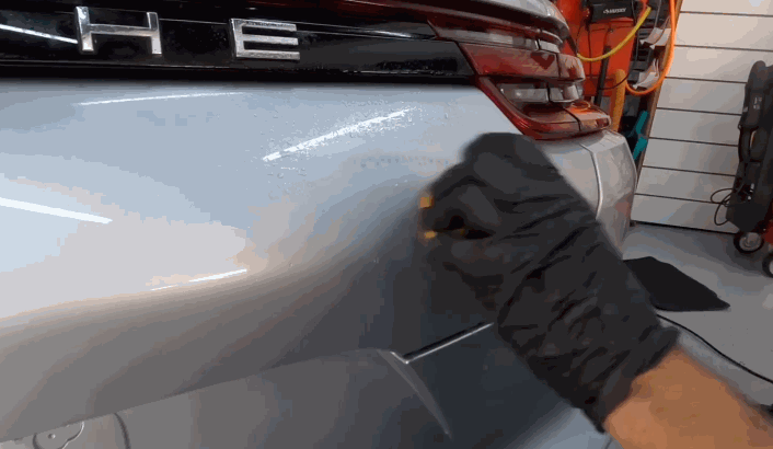 Person in gloves removing ceramic coating from the rear bumper of a Porsche with a circular wiping motion.