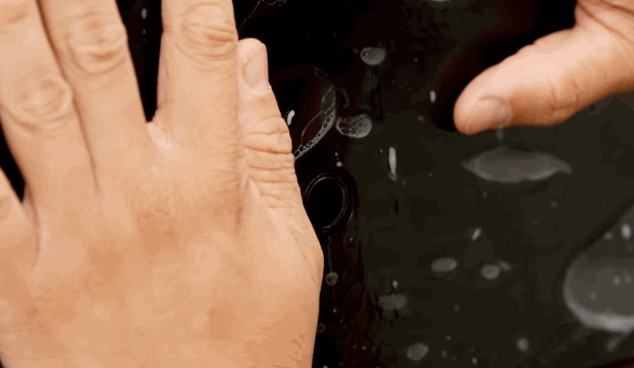 Two hands pressing and smoothing a paint protection film onto a car panel, ensuring it adheres without bubbles.