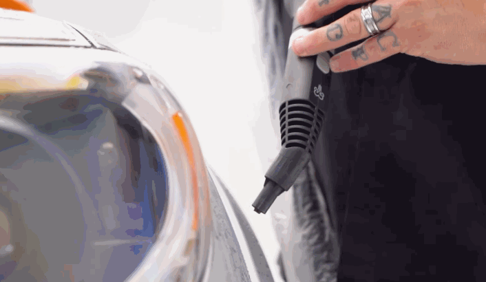 Close-up of a heat gun being used to apply PPF smoothly around a car headlight, ensuring a tight and seamless fit.