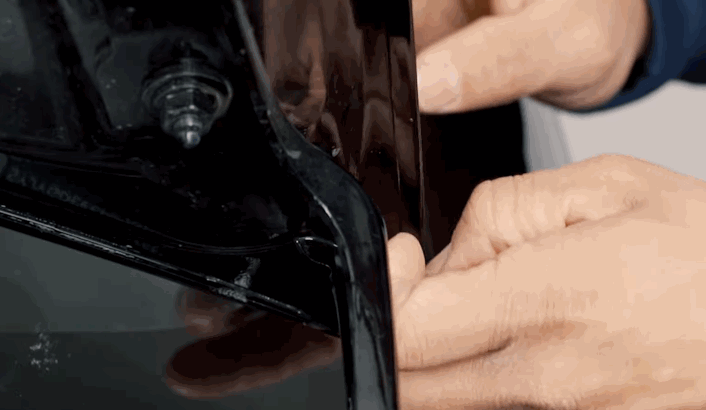 Close-up of a technician carefully tucking PPF into the edge of a black car panel near the headlight housing.