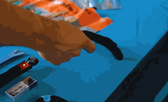 A person selects tools from a table covered with graphic installation gear, including squeegees, blades, and decals, used for applying commercial fleet graphics.