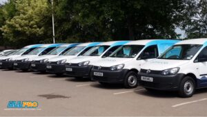 A row of white commercial vans with blue branded graphics parked in a lot, all featuring matching designs on the hoods and sides.