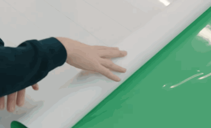 A person rolls out a large sheet of white vinyl over a bright green surface, preparing material for commercial fleet graphics application.