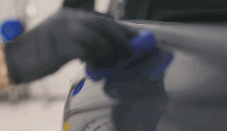 Technician wearing black gloves uses a heat gun to shape Paint Protection Film over a vehicle surface. The close up shows the film being carefully molded and smoothed to ensure a seamless protective finish.