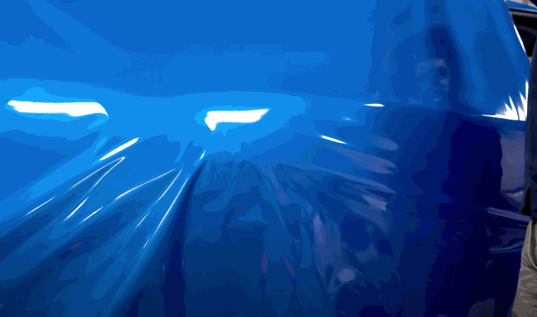 Close up of glossy blue vinyl wrap stretched smoothly across a vehicle panel highlighting the reflective surface and seamless application.