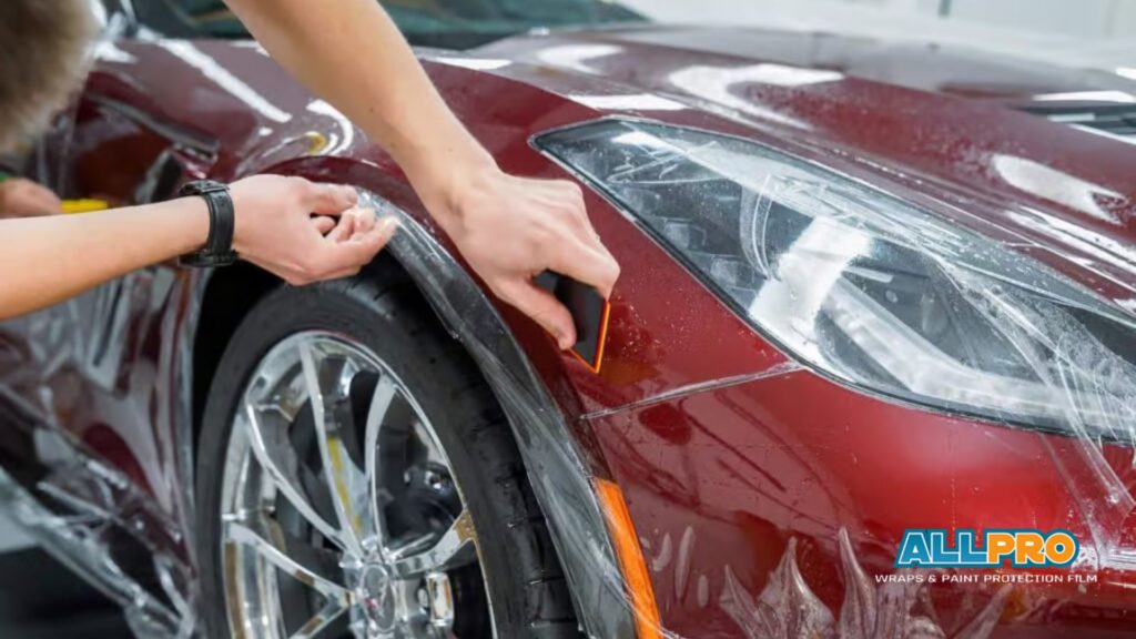 Installer uses a squeegee tool to smooth Paint Protection Film across the front fender of a red sports car removing water and air bubbles.