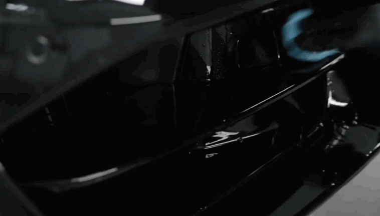 Close up of a sleek black car surface reflecting light with a smooth mirror like finish in a dark setting. The clean and polished panel highlights the results of ceramic coating for enhanced depth and protection.