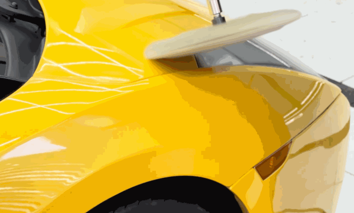 A rotary buffer polishes a bright yellow car panel, restoring a glossy finish as part of a car detailing process focused on paint correction. The smooth surface reflects overhead lights, showing a high shine result.