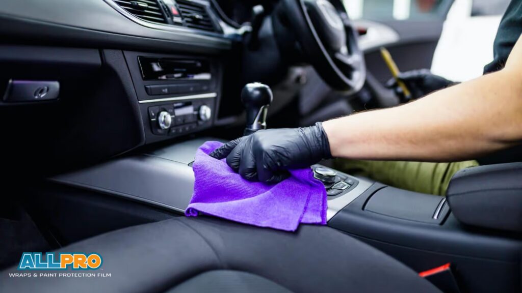 Gloved hand wiping a car center console with a purple microfiber cloth during car detailing.