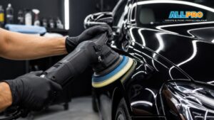 A technician uses a machine polisher on the front fender of a glossy black vehicle during car detailing.
