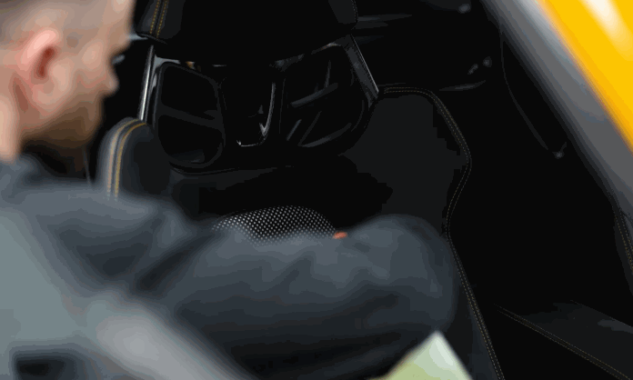 A technician cleans the dark interior of a vehicle during car detailing. The close up shows attention to the rear console and upholstery areas.