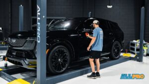 Technician applies ceramic coating to a black SUV on a lift inside a clean detailing shop.