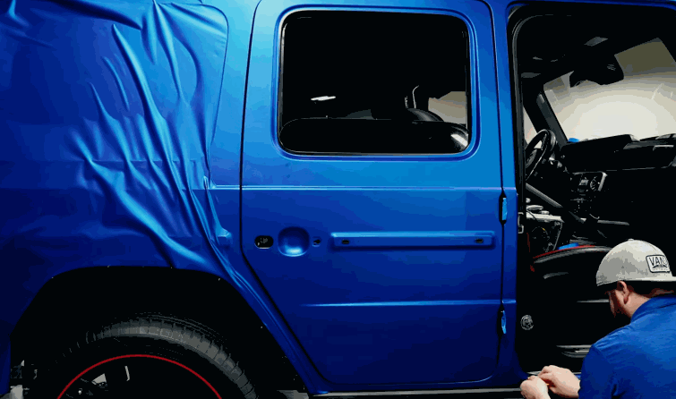 Blue vinyl wrap covers the side of a Jeep with the rear panel still wrinkled before smoothing.
