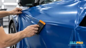 Installer smooths blue vinyl wrap across a vehicle door with a squeegee.