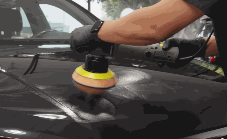 Detailer uses a machine polisher on a black vehicle panel to refine the paint before ceramic coating application.